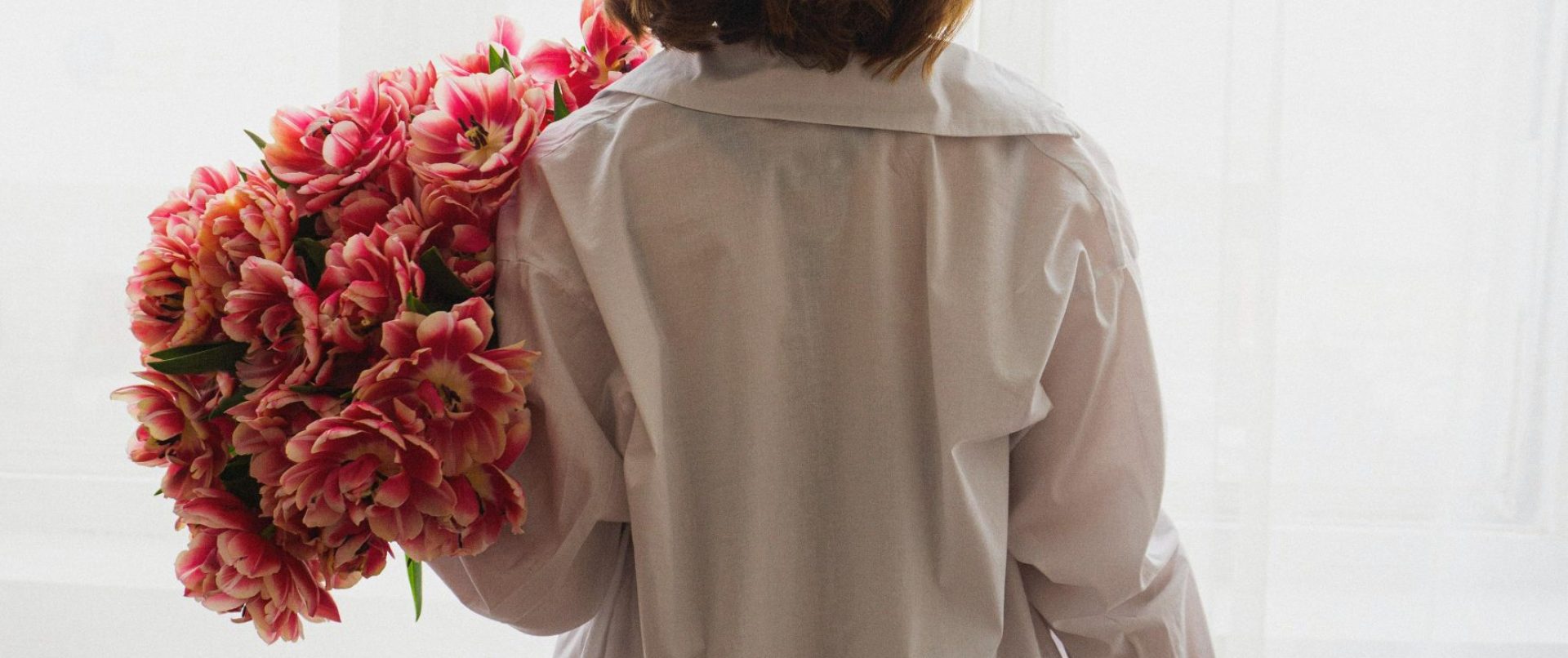 Close-up of a woman wearing a white shirt, a wineglass and a bouquet of flowers.